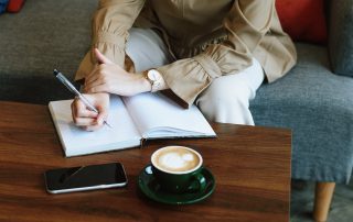 Woman sitting at coffee table with notebook and coffee.