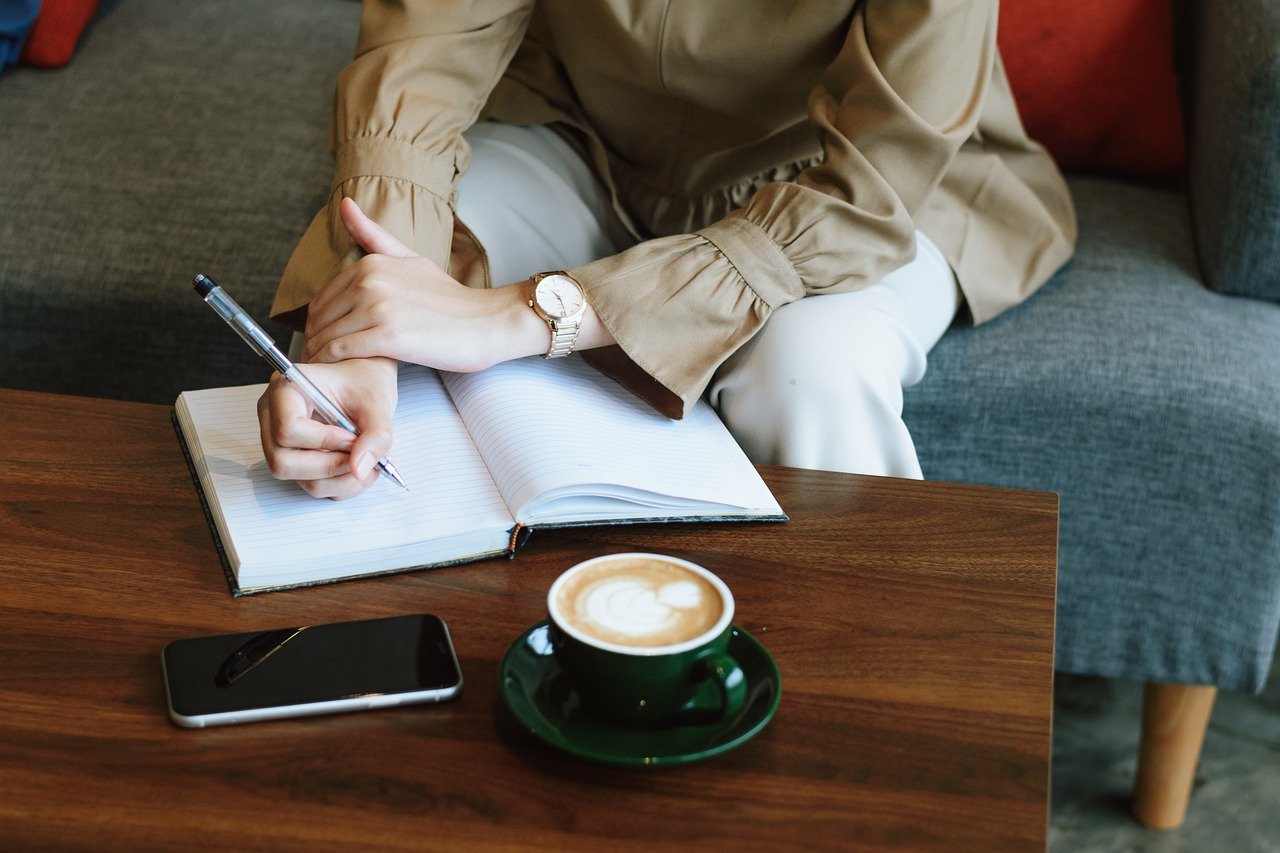 Woman sitting at coffee table with notebook and coffee.